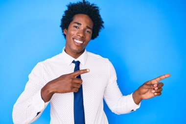 Afro saçlı, iş gömleği ve kravat takan, gülümseyen ve kameraya bakan, iki eli ve parmağı yanda olan yakışıklı Afro-Amerikalı bir adam.. 