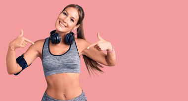 Güzel İspanyol bir kadın spor kıyafetleri giyiyor ve kulaklık takıyor. Kendine güvenen, gülümseyen, gururlu ve mutlu birini işaret ediyor.. 