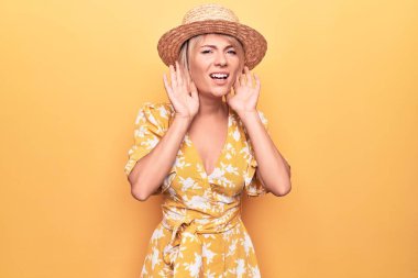 Yaz şapkası takıp sarı arka planda giyinen güzel sarışın kadın iki elini de kulak hareketi yaparken duymaya çalışıyor. Dedikoduya meraklı. İşitme problemi, sağır