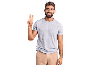 Gündelik kıyafetler giyen genç İspanyol adam üç numarayı gösterip işaret ederken kendinden emin ve mutlu gülümsüyor.. 