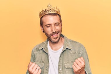 Kral tacı takan yakışıklı genç adam şaşkınlık ve şaşkınlık içinde kollarını kaldırarak ve gözlerini kapayarak zaferi kutluyor. 