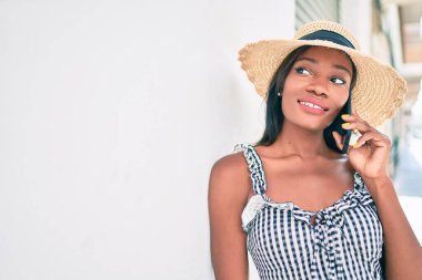 Genç Afrikalı Amerikalı kadın tatilde. Akıllı telefondan konuşuyor. Şehrin sokağında duvara yaslanıyor.