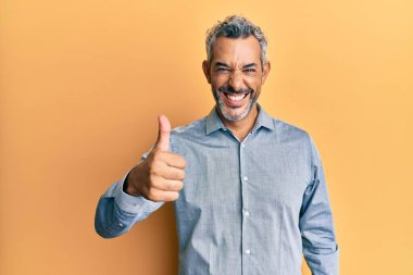 Orta yaşlı, gri saçlı, günlük kıyafetler giyen mutlu ve pozitif gülümseyen, başparmağıyla mükemmel ve onay işareti yapan bir adam. 
