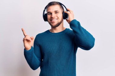 Genç yakışıklı adam kulaklık takarak müzik dinliyor. Gülümsüyor, mutlu bir şekilde işaret ediyor. 