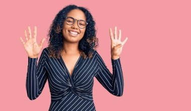 Genç Afro-Amerikalı kadın, günlük kıyafetler ve gözlük takıyor ve dokuz numaralı parmaklarıyla işaret ediyor, gülümsüyor ve mutlu.. 