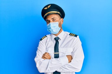 Sakallı, uçak pilotu üniforması giyen, güvenlik maskesi takan, kuşkucu ve gergin, yüzünde çapraz kollu tasvip etmeyen yakışıklı bir adam. negatif kişi. 