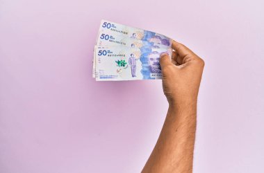 İspanyol el, 50 Kolombiya pezosu tutuyor. İzole edilmiş pembe arka planda..