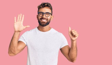 Gündelik kıyafetler giyen ve gözlük takan İspanyol genç adam altı numarayı gösterip işaret ederken kendinden emin ve mutlu gülümsüyor.. 