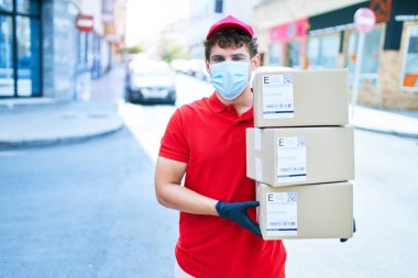 Coronavirus koruması takan beyaz bir kurye elinde karton paketler, şehirde yürüyor..