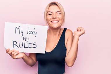 Genç sarışın kadın, kadınların özgürlüğünü istiyor. Bedenimle kağıt tutuyor. Benim kurallarım gururla bağırıyor, zaferi kutluyor ve kollarını kaldırarak çok heyecanlı.