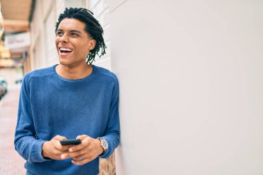 Genç Afrikalı Amerikalı mutlu gülümsüyor. Duvara dayanmış akıllı telefon kullanıyor..