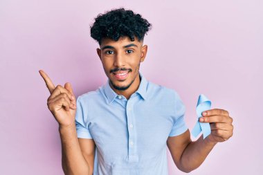 Genç Arap yakışıklı adam mavi kurdele tutuyor gülümsüyor mutlu eli ve parmağı yana bakıyor 