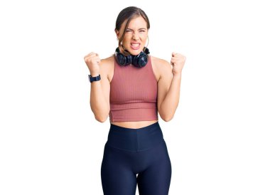 Güzel beyaz kadın spor kıyafetleri giyiyor ve kulaklık takıyor kızgın ve kızgın yumruklar sallıyor öfkeyle bağırırken. öfke ve agresif konsept. 