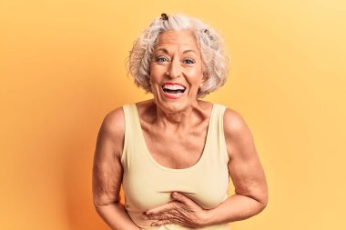 Kıdemli gri saçlı kadın, günlük kıyafetler giyiyor, gülümsüyor ve kahkahalarla gülüyor.. 