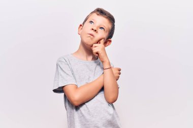 Hoş sarışın çocuk gündelik kıyafetler giyiyor ciddi bir yüz ifadesi var eli çenesinde soru soran, kafa karıştırıcı bir fikir hakkında düşünceli 