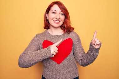 Genç, güzel, kızıl saçlı bir kadın, sarı arka planda kalbi olan, gündelik bir kazak giyiyor. Gülümsüyor ve kameraya bakıyor. İki eliyle ve parmaklarıyla onu işaret ediyor..