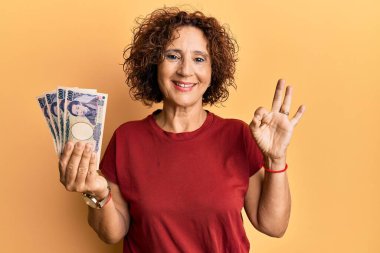 Güzel, orta yaşlı, olgun bir kadın elinde 5000 Japon banknotu tutuyor. Parmaklarıyla imza atıyor, gülümsüyor ve mükemmel bir sembol oluşturuyor. 