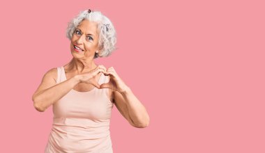 Yaşlı, gri saçlı, sıradan kıyafetler giyen, aşkla gülümseyen, kalp sembolü ve elleri olan bir kadın. romantik kavram. 