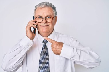 Kıdemli gri saçlı adam iş kıyafetleri giymiş akıllı telefondan konuşuyor mutlu bir şekilde el ve parmağıyla işaret ediyor. 