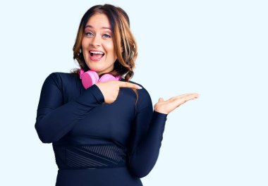 Spor kıyafetleri giyen, kulaklık takan, kameraya hayret içinde gülümseyen, eli ve parmağı olan güzel beyaz bir kadın.. 