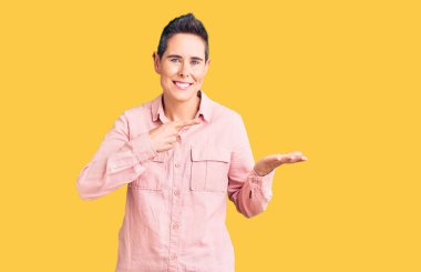 Kısa saçlı, sıradan kıyafetler giyen genç bir kadın kameraya hayret ediyor ve gülümsüyor.. 