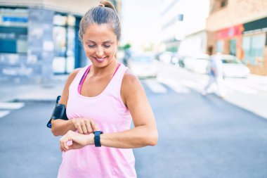 Şehirdeki orta yaşlı sporcu kadın gülümseyerek antrenman yapıyor.