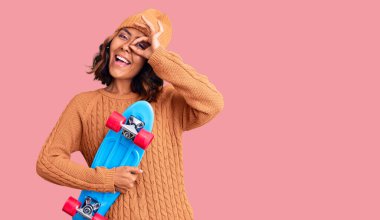 Genç, güzel, melez bir kadın gülümseyen bir kaykay tutuyor. 