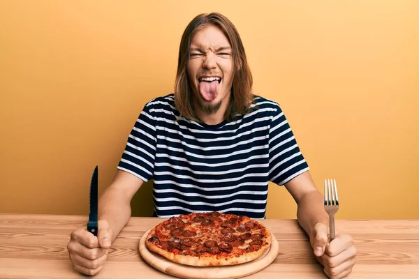 英俊的白种人 吃着美味的意大利辣披萨 伸出舌头 满脸滑稽的表情 — 图库照片
