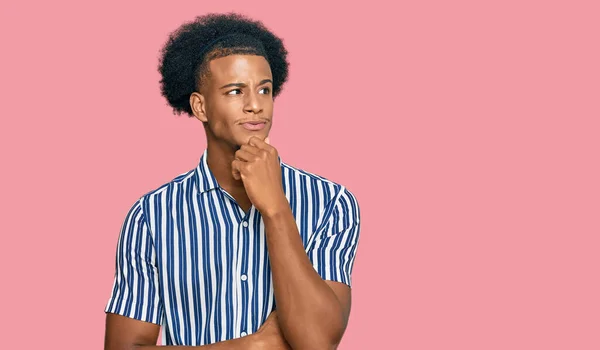 African american man with afro hair wearing casual clothes serious face thinking about question with hand on chin, thoughtful about confusing idea