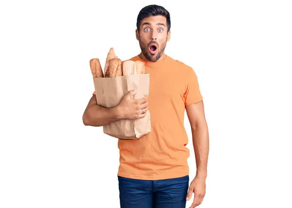 Junger Hispanischer Mann Hält Papiertüte Mit Brot Der Hand Erschrocken — Stockfoto