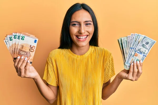 Young brunette woman holding bunch of dollars and euros smiling and laughing hard out loud because funny crazy joke.