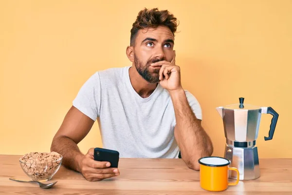 Joven Hombre Hispano Sentado Mesa Desayunando Usando Teléfono Inteligente Cara — Foto de Stock