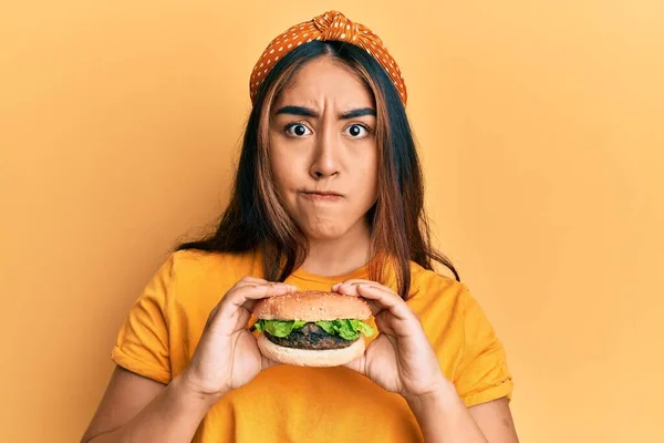 Young Latin Woman Eating Tasty Classic Burger Skeptic Nervous Frowning — Stock Photo, Image