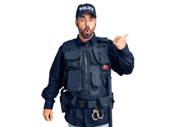 Young hispanic man wearing police uniform surprised pointing with hand finger to the side, open mouth amazed expression.