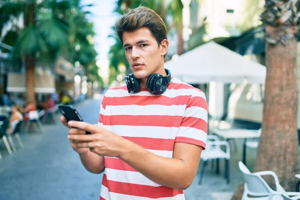Νεαρός Καυκάσιος Άνδρας Σοβαρή Έκφραση Χρησιμοποιώντας Smartphone Και Ακουστικά Στην — Φωτογραφία Αρχείου