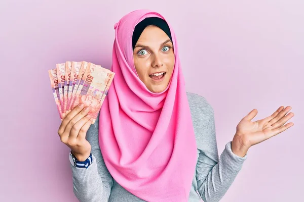 年轻的高加索女人头戴伊斯兰头巾 手持南非兰特钞票 笑容满面 高举双手庆祝胜利 — 图库照片