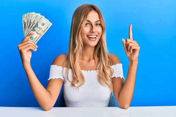 Piękna Blondynka Młoda Kobieta Trzymająca Banknoty Dolarów Uśmiechająca Się Pomysłem — Zdjęcie stockowe