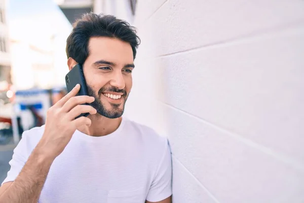 若いヒスパニック系の男笑顔幸せな話でスマートフォンの壁にもたれて — ストック写真