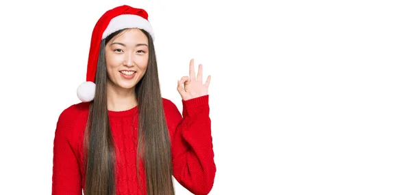 若い中国の女性は手と指でOkサインを行う肯定的な笑顔クリスマスの帽子を着用 成功した表現 — ストック写真