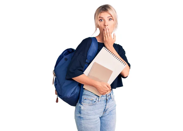 若い美しいブロンドの女性は 学生のバックパックを手で口をカバーノートブックを保持着てショックを受け ミスを恐れている 驚きの表情 — ストック写真