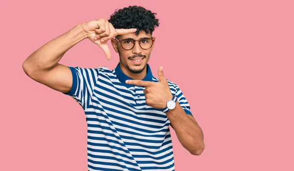 年轻的阿拉伯男子 身穿休闲装 戴着眼镜 面带微笑 用手和手指做框架 面带微笑 创意与摄影概念 — 图库照片