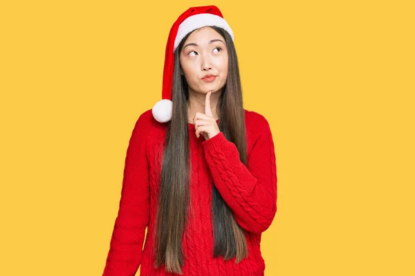 若いです中国の女性身に着けていますクリスマス帽子考え濃縮約疑問について指で顎と見上げ疑問に思って — ストック写真