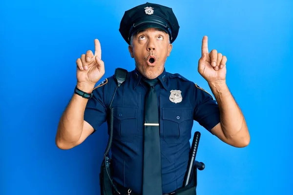Handsome middle age mature man wearing police uniform amazed and surprised looking up and pointing with fingers and raised arms.