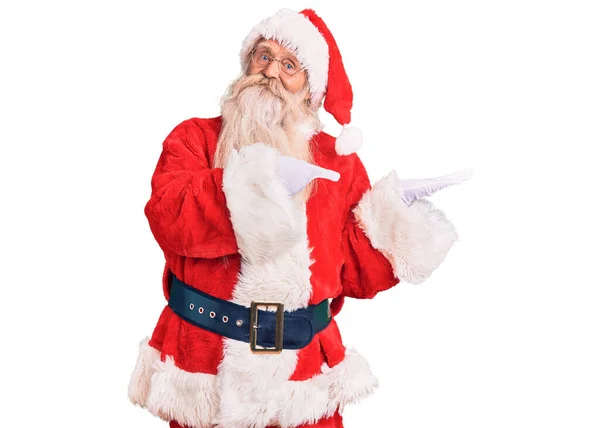 年长的老人 头发灰白 长胡子 身穿传统的圣诞老人服装 一边手牵着手 一边指指点点着镜头 一边惊讶地微笑着 — 图库照片