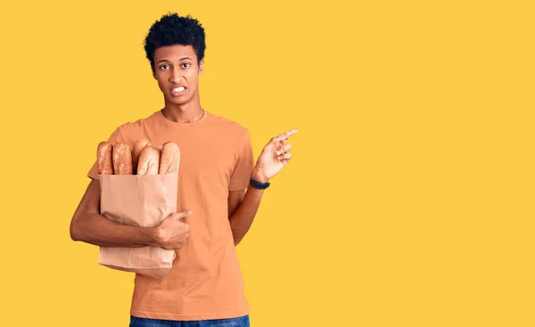 Mladý Africký Američan Držící Papírový Sáček Chlebem Ukazující Stranou Ustaraný — Stock fotografie