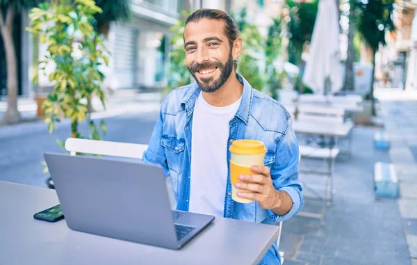Young middle eastern man smiling happy working using laptop at coffee shop terrace.