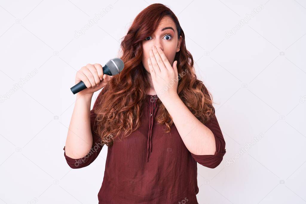 Young beautiful woman singing song using microphone covering mouth with hand, shocked and afraid for mistake. surprised expression 