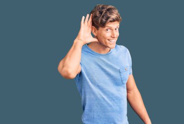 Gündelik kıyafetler giyen genç yakışıklı adam, kulağı kulağında gülümseyerek dedikoduları ve dedikoduları dinliyor. Sağırlık kavramı. 