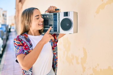 Genç, güzel, sarışın, beyaz bir kadın güneşli bir günde gülerek teypte müzik çalıyor.