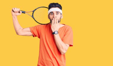 Sakallı, tenis oynayan, ağzı ağızla kapalı raket tutan ve hata yapmaktan korkan genç yakışıklı bir adam. şaşırmış ifade 